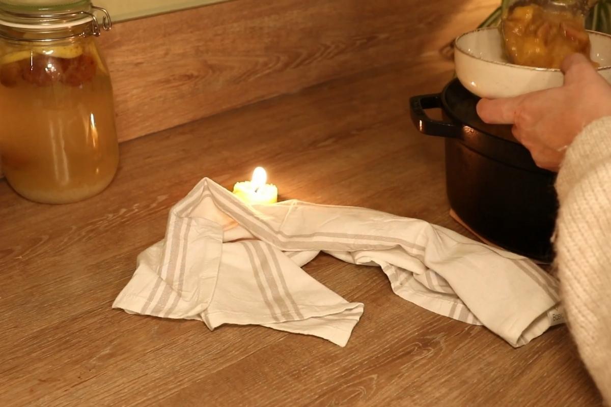 Upaljena sveća na kuhinjskom pultu uz krpu i šerpu stvara prijatnu, toplu atmosferu