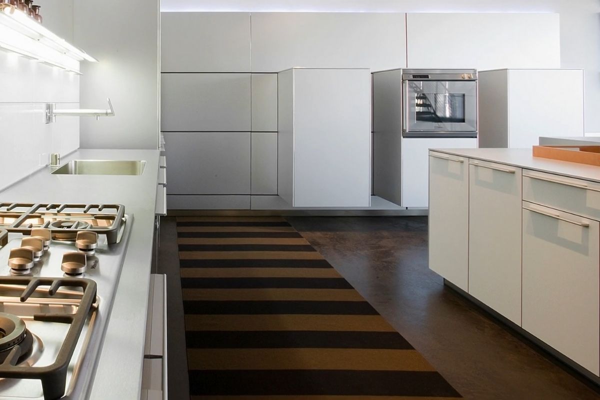 Minimalistička bela kuhinja u kojoj centralno mesto zauzima prugasta podna staza u toplim tonovima